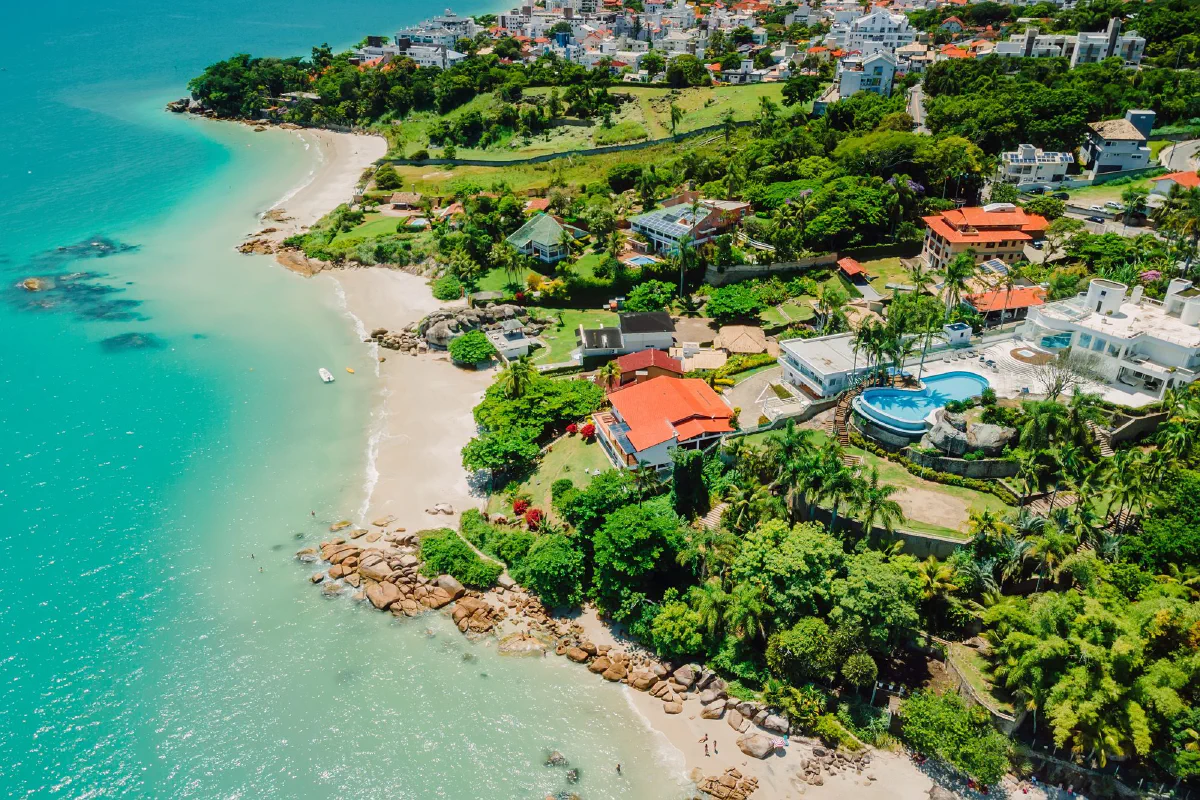 Praia de água calma e turquesa com casas à beira-mar em Florianópolis (SC)
