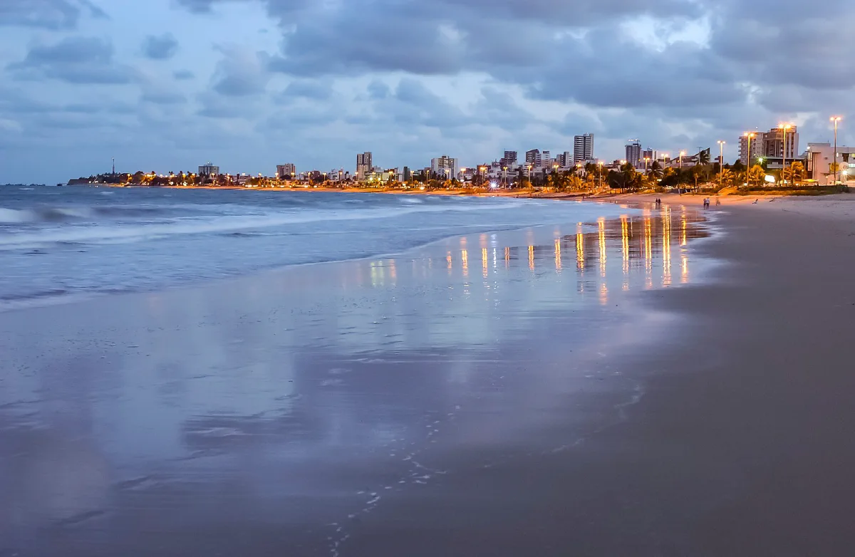 Praia de João Pessoa (PB) ao anoitecer, com as luzes dos prédios refletidas na areia molhada