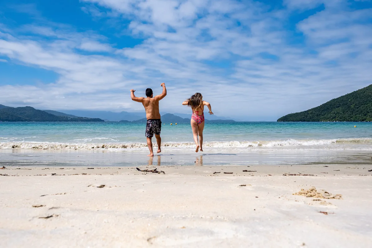 Casal correndo na areia de uma praia da Ilha Anchieta, em Ubatuba (SP)