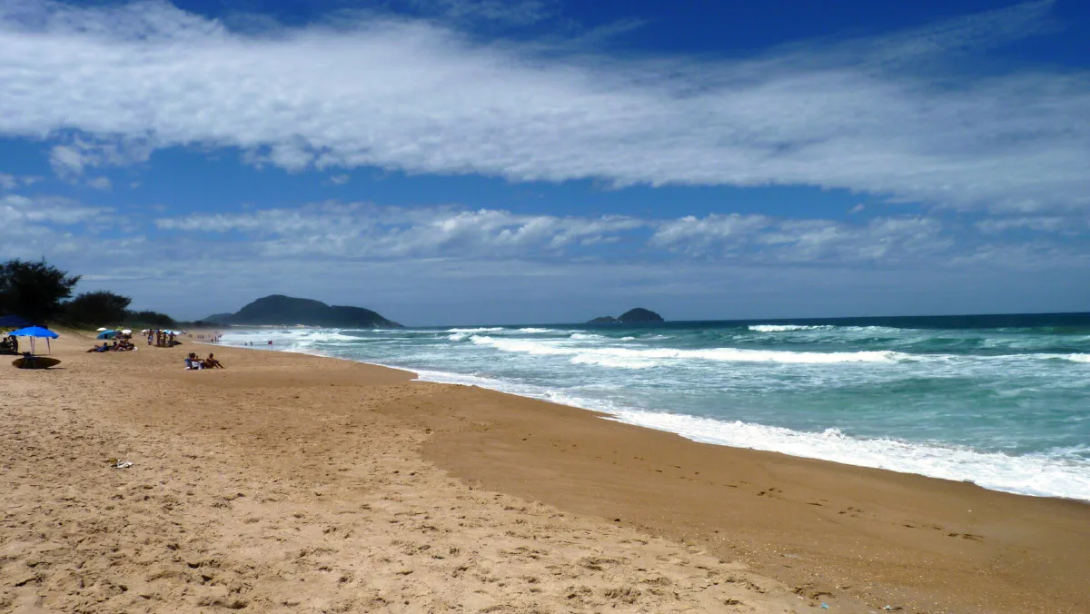 Praia longa com ondas quebrando e poucas pessoas na areia.