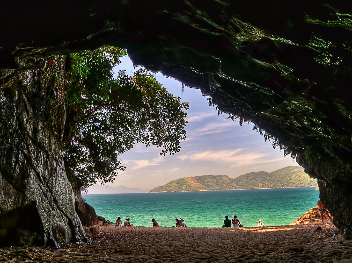 Abertura da Gruta que Chora vista de dentro, com vegetação na rocha e a Praia da Sununga ao fundo.