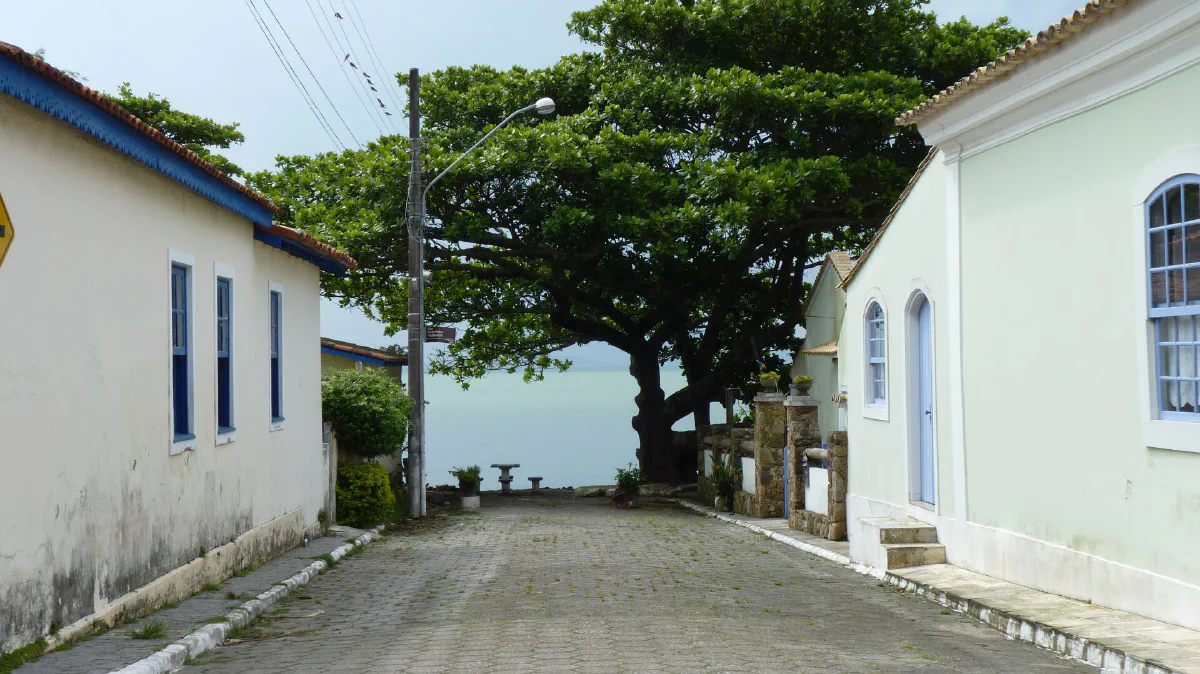 Rua de um povoado terminando na água, com morros ao fundo.