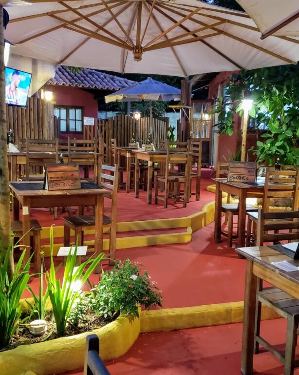 restaurante Boiteko com várias mesas de madeira sob um chão vermelho em Arraial d’Ajuda na Bahia