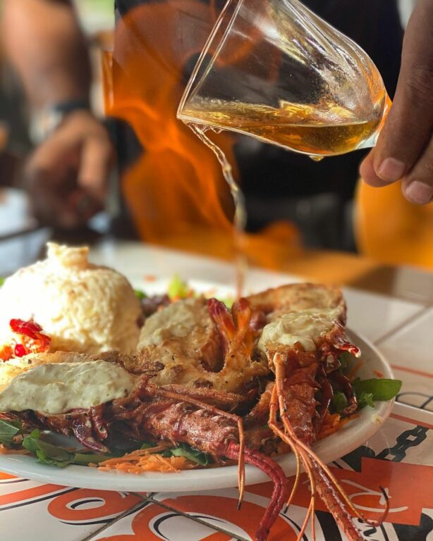 líquido avermelhado sendo derramado em cima da lagosta na Vovó Bela Restaurante em Porto Seguro na Bahia